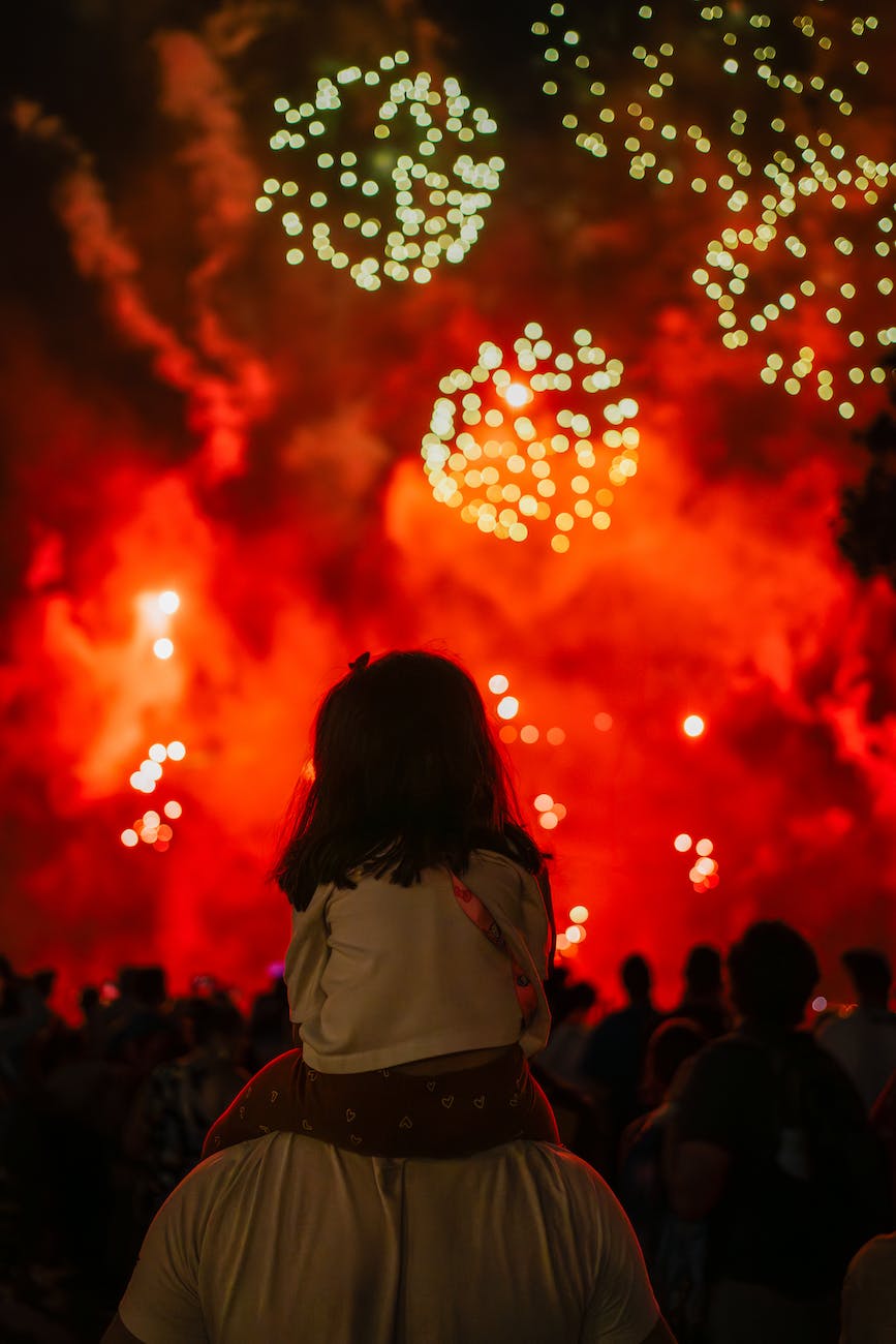 back view of a man holding a girl on his shoulders on the background of firework display